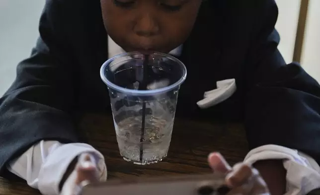 Legend McNeary, 4, takes a sip of water while sitting inside between bridal party photos before a wedding Saturday, Aug. 23, 2025, in Newtown, Ohio. (AP Photo/Joshua A. Bickel)