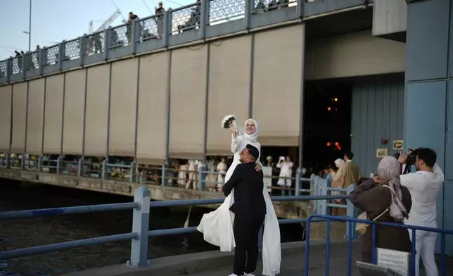 Sude Keles, top, and her husband Suat Keles pose during a photo session at Galata bridge in Istanbul, Turkey, Thursday, July 31, 2025. (AP Photo/Emrah Gurel)
