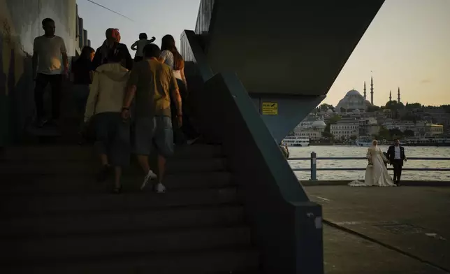 A couple wearing their wedding outfits pose during a photo session at Galata bridge, in Istanbul, Turkey, Wednesday, July 30, 2025. (AP Photo/Emrah Gurel)