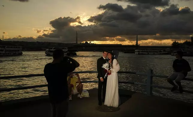 Damla Avci, right, and her husband Mustafa Ertan pose during a photo session at Galata bridge in Istanbul, Turkey, Thursday, July 31, 2025. (AP Photo/Emrah Gurel)