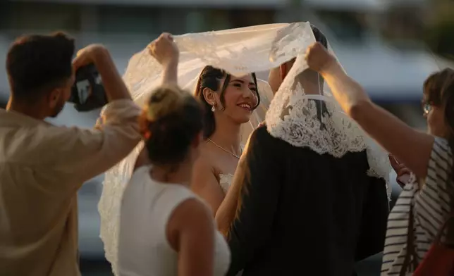 A couple wearing their wedding outfits pose during a photo session at Galata bridge, in Istanbul, Turkey, Wednesday, July 30, 2025. (AP Photo/Emrah Gurel)