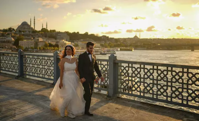 A couple wearing their wedding outfits walk along Galata bridge during a photo session, in Istanbul, Turkey, Thursday, July 31, 2025. (AP Photo/Emrah Gurel)