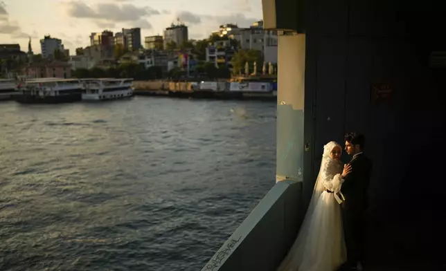 A couple wearing their wedding outfits pose during a photo session at Galata bridge, in Istanbul, Turkey, Wednesday, July 30, 2025. (AP Photo/Emrah Gurel)