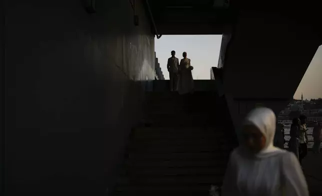 A couple wearing their wedding outfits arrive for a photo session at Galata bridge, in Istanbul, Turkey, Monday, July 28, 2025. (AP Photo/Emrah Gurel)