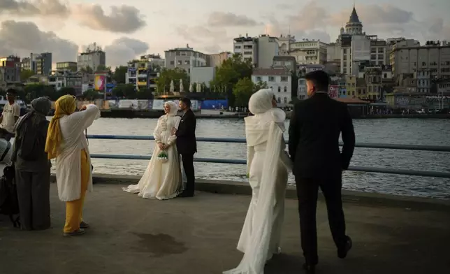 Couples wearing their wedding outfits pose during a photo session at Galata bridge, in Istanbul, Turkey, Wednesday, July 30, 2025. (AP Photo/Emrah Gurel)