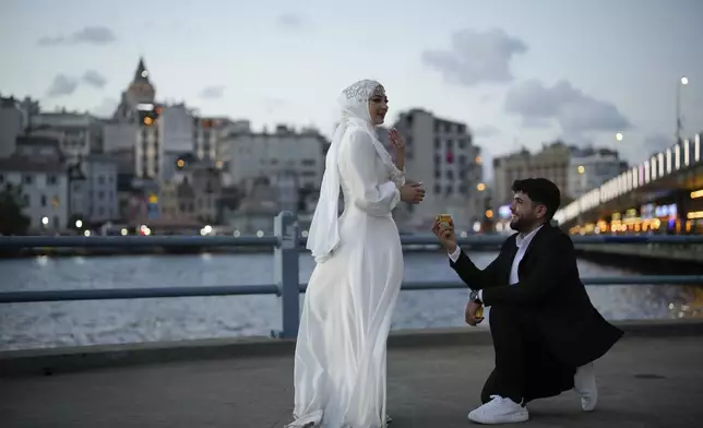 Halil Ibrahim Ucucu, right, and his wife Hasret Yilmaz Ucucu wearing their wedding outfits pose for a photo session at Galata bridge, in Istanbul, Turkey, Thursday, July 31, 2025. (AP Photo/Emrah Gurel)