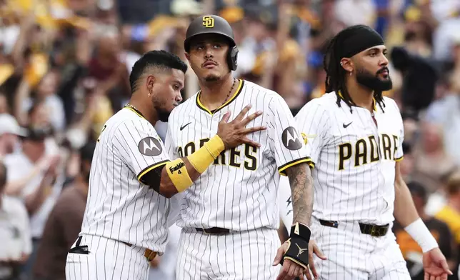 San Diego Padres' Manny Machado, center, is congratulated by Luis Arraez, left, after scoring on a single by Ramon Laureano against the Los Angeles Dodgers in the fourth inning of a baseball game Saturday, Aug. 23, 2025, in San Diego. (AP Photo/Derrick Tuskan)