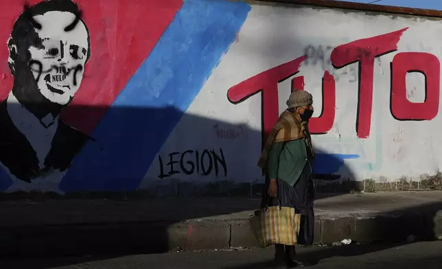 A woman stands in front of a defaced mural promoting presidential candidate Jorge "Tuto" Quiroga of the Alianza Libre political party, in El Alto, Bolivia, Saturday, Aug. 9, 2025. (AP Photo/Juan Karita)