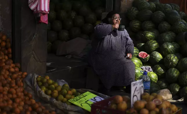 A fruit vendor watches supporters of presidential candidate Samuel Doria Medina pass by during a campaign rally five days ahead of presidential elections, in La Paz, Bolivia, Tuesday, Aug. 12, 2025. (AP Photo/Natacha Pisarenko)