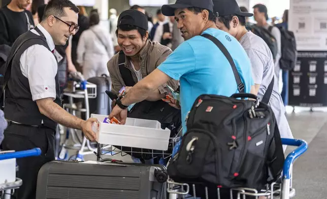 An Air Canada employee hands out snacks to travellers waiting for a flight at Montreal-Pierre Elliott Trudeau International Airport in Dorval, Que., on Tuesday, Aug. 19, 2025. (Christinne Muschi/The Canadian Press via AP)