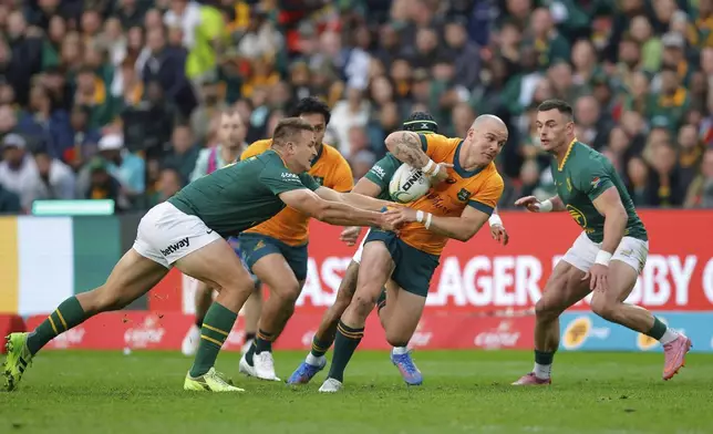 Australia's Dylan Pietsch, centre, being tackled by South Africa's Andre Esterhuizen, left, during a rugby championship test match between South Africa and Australia, at Ellis Park stadium in Johannesburg, South Africa, Saturday, Aug. 16, 2025. (AP Photo/Frans Lombard)