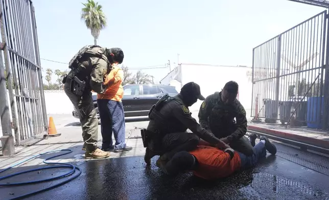 Immigration agents detain two men at a car wash on Friday, Aug. 15, 2025, in Montebello, Calif. (AP Photo/Gregory Bull)