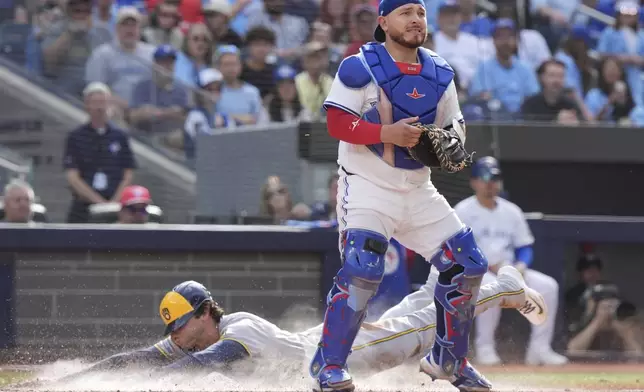 Toronto Blue Jays catcher Alejandro Kirk (30) looks for the ball as Milwaukee Brewers outfielder Christian Yelich (22) scores behind him during seventh inning MLB baseball action in Toronto on Saturday, August 30, 2025. (Frank Gunn/The Canadian Press via AP)