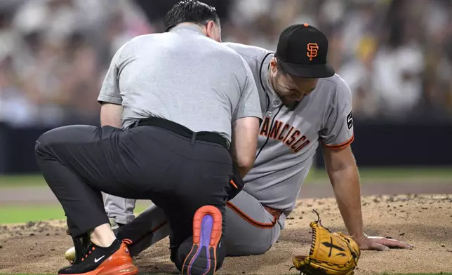 San Francisco Giants starting pitcher Landen Roupp, right, is checked by a trainer after being hit by a line drive during the third inning of a baseball game against the San Diego Padres Wednesday, Aug. 20, 2025, in San Diego. (AP Photo/Orlando Ramirez)