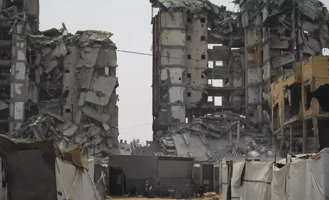 A group of Palestinians sit in the shade of their tent amid destroyed buildings on a hot summer day in Gaza City, Tuesday, Aug. 12, 2025. (AP Photo/Jehad Alshrafi)