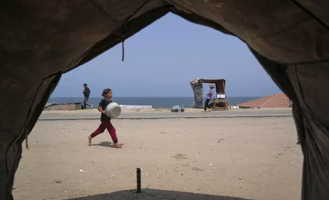 A Palestinian girl carries an empty basin as she runs to a water distribution point during a hot summer day with temperatures reaching 36 °C (97 °F) in Deir al-Balah, in the central Gaza Strip, Wednesday, Aug. 13, 2025. (AP Photo/Abdel Kareem Hana)