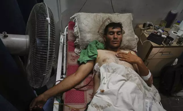 A Palestinian patient seeks relief from the heat by sitting near a fan during a heat wave, inside a warehouse set up in the yard of Shifa Hospital in Gaza City, Wednesday, Aug. 13, 2025. (AP Photo/Jehad Alshrafi)