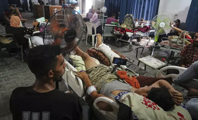 Palestinian patients seek relief from the heat by sitting near a fan during a heat wave, inside a warehouse set up in the yard of Shifa Hospital in Gaza City, Wednesday, Aug. 13, 2025. (AP Photo/Jehad Alshrafi)