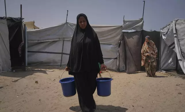 Displaced Palestinian Rana Odeh, carries buckets full of water in the next to where she takes shelter in Muwasi, Khan Younis, Gaza Strip, Wednesday, Aug, 13, 2025. (AP Photo/Abdel Kareem Hana)
