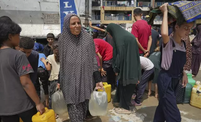 In the summer heat, Enaam Al Majdoub carries a jerrycan after collecting water from a distribution point in Gaza City, Tuesday, Aug. 12, 2025. (AP Photo/Jehad Alshrafi)