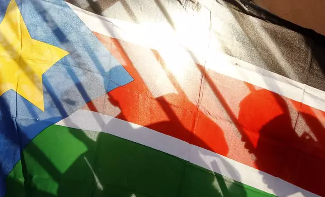 FILE - The silhouettes of South Sudanese people are seen through a South Sudanese flag as they line up to cast their votes in Juba, South Sudan, on Jan. 9, 2011. (AP Photo/Jerome Delay, File)