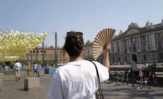 A woman uses a fan to cool off Tuesday, Aug. 12, 2025 in Toulouse, southwestern France. (AP Photo/Fred Scheiber)