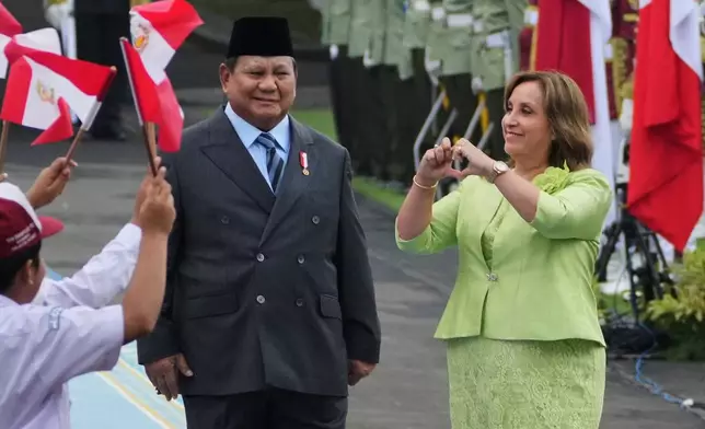 Peruvian President Dina Boluarte, right, gives a love symbol at children waving Indonesian and Peruvian flags as his Indonesian counterpart Prabowo Subianto looks on during a welcoming ceremony prior to their meeting at Merdeka Palace in Jakarta, Indonesia, Monday, Aug. 11, 2025. (AP Photo/Achmad Ibrahim)