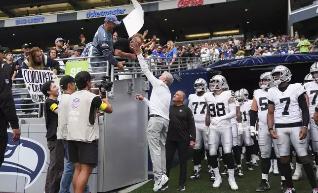 Las Vegas Raiders head coach Pete Carroll, center, tries to grab a sign that reads "Bigger Bust-Geno or JaMarcus Russell?" before an NFL preseason football game against the Seattle Seahawks, Thursday, Aug. 7, 2025, in Seattle. (AP Photo/Lindsey Wasson)