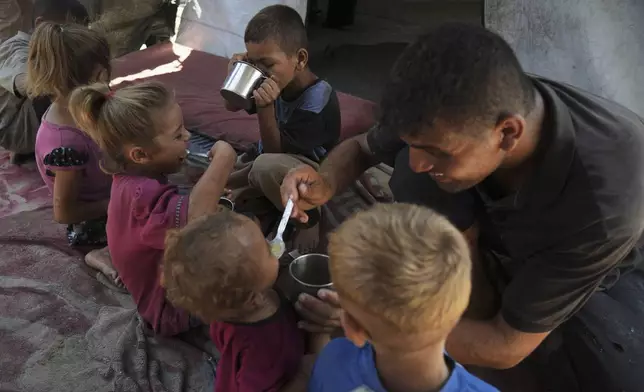 Fadi Sobh gives lentil soup to his children as they sit in their tent at a camp for displaced Palestinians in Gaza City, July 24, 2025. (AP Photo/Jehad Alshrafi)