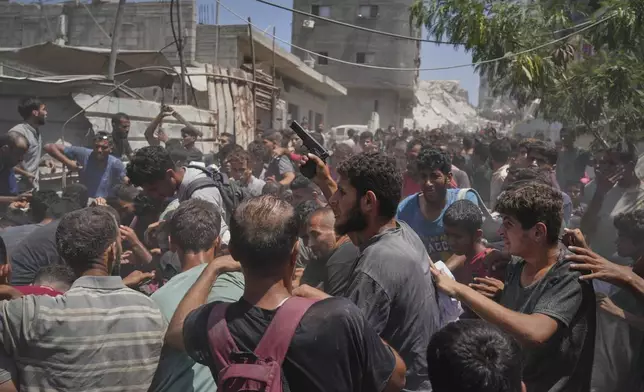 A Palestinian man waves a pistol as others struggle to collect humanitarian aid airdropped into Gaza City, northern Gaza Strip, Aug. 7, 2025. (AP Photo/Jehad Alshrafi)