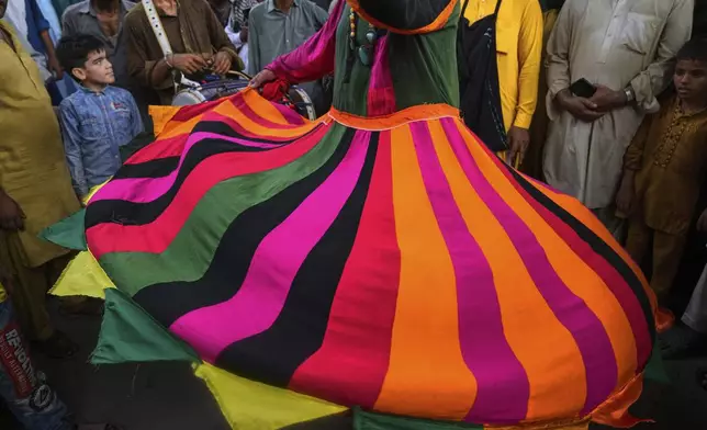 Youngsters with others look to a spiritual path devotee locally called 'Malang' performing a devotional dance called 'Dhamaal' during the celebrations of the three-day annual festival or 'Urs' of famous saint Hazrat Ali Hajveri, popularly known as Data Ganj Bakhsh at his shrine, in Lahore, Pakistan, Wednesday, Aug. 13, 2025. (AP Photo/K.M. Chaudary)