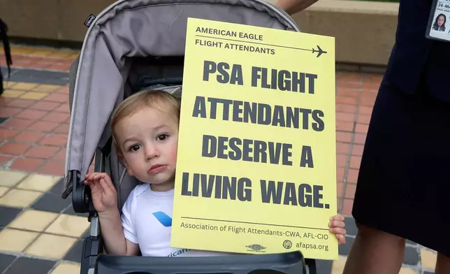 A child is seen with a placard as PSA Airlines flight attendants hold a demonstration at Ronald Reagan Washington National Airport, Monday, August 18, 2025, in Washington. (AP Photo/Rahmat Gul)