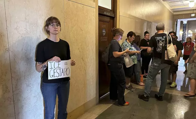 Emily Pietrzak holds a sign that reads "ICE=Gestapo" as other protesters gather outside the Nebraska governor's office in Lincoln, Neb., Tuesday, Aug. 19, 2025. "I believe our government is hurting people who live in our country and I think we should stand up for each other," she said. (AP Photo/Josh Funk)