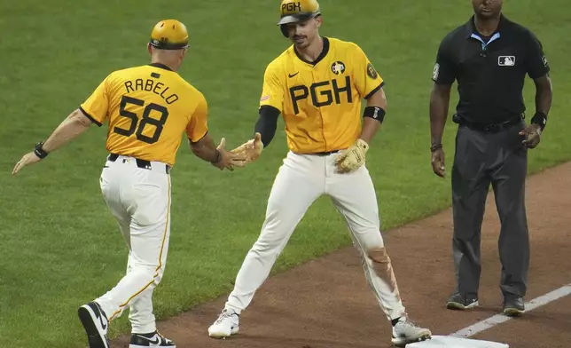 Pittsburgh Pirates' Bryan Reynolds, center, celebrates with third base coach Mike Rabelo (58) as Reynolds stands on third base after driving in two runs with a triple off Cincinnati Reds pitcher Tony Santillan during the eighth inning of a baseball game in Pittsburgh, Friday, Aug. 8, 2025. (AP Photo/Gene J. Puskar)