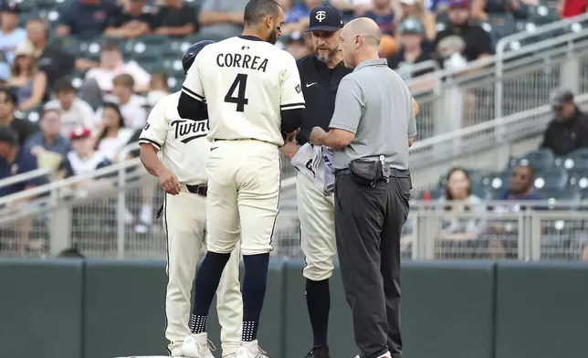 Minnesota Twins Carlos Correa (4) talks with manager Rocco Baldelli and head athletic trainer Nick Paparesta after hitting a single against the Boston Red Sox during the first inning of baseball game Tuesday, July 29, 2025, in Minneapolis. Correa left the game with an illness. (AP Photo/Matt Krohn)