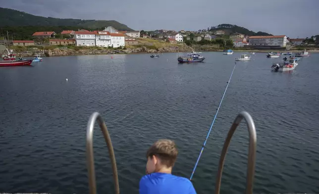 A young boy waits to catch a fish Tuesday, June 24, 2025, in Lira, Spain. (AP Photo/Annika Hammerschlag).