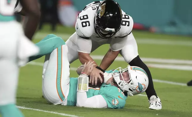 Miami Dolphins quarterback Quinn Ewers (14) is sacked by Jacksonville Jaguars defensive end Ethan Downs (96) during the second half of an NFL preseason football game, Saturday, Aug. 23, 2025, in Miami Gardens, Fla. (AP Photo/Lynne Sladky)