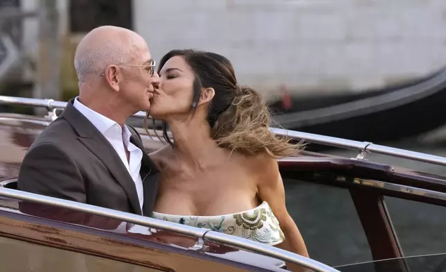 FILE - Jeff Bezos, left, and Lauren Sanchez kiss as they leave a hotel for their pre wedding reception, in Venice, Italy, June 26, 2025. (AP Photo/Luca Bruno, File)