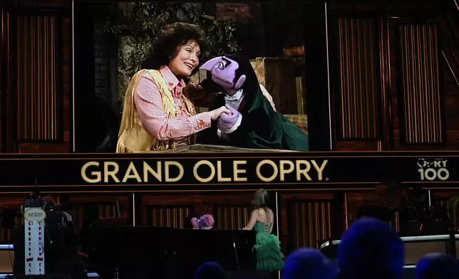 A video of Loretta Lynn and Count von Count of Sesame Street is displayed as puppet Abby Cadabby and Tayla Lynn, below, perform at the Grand Ole Opry, Thursday, Aug. 14, 2025, in Nashville, Tenn. (AP Photo/George Walker IV)