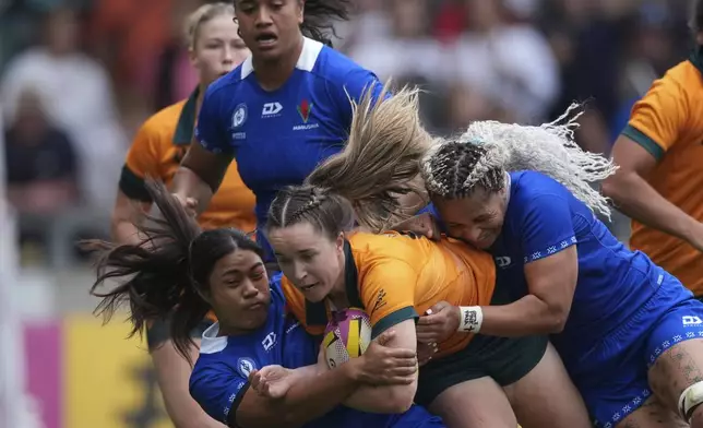 Cecilia Smith of Australia, center, is tackled by Sui Pauaraisa of Samoa during the group A match at the 2025 Women's Rugby World Cup between Australia and Samoa in Manchester, England, Saturday, Aug. 23, 2025. (AP Photo/Dave Shopland)