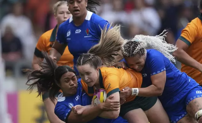 Tia Hinds of Australia, center, is tackled by Sui Pauaraisa of Samoa during the group A match at the 2025 Women's Rugby World Cup between Australia and Samoa in Manchester, England, Saturday, Aug. 23, 2025. (AP Photo/Dave Shopland)