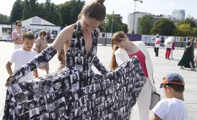 Antanina Kanavalava, center right, a former political prisoner in Belarus, looks at photos of other prisoners printed on a dress at the Freedom March for Belarus in Warsaw, Poland, on Saturday, Aug. 9, 2025. (AP Photo/Czarek Sokolowski)