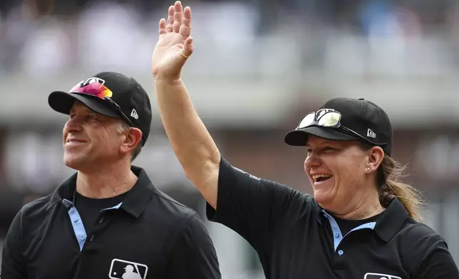 Umpires Chris Guccione, left, and Jen Pawol, right, react to fans in the crowd at the conclusion of the first baseball game of a doubleheader between the Atlanta Braves and Miami Marlins, Saturday, Aug. 9, 2025, in Atlanta. (AP Photo/Colin Hubbard)