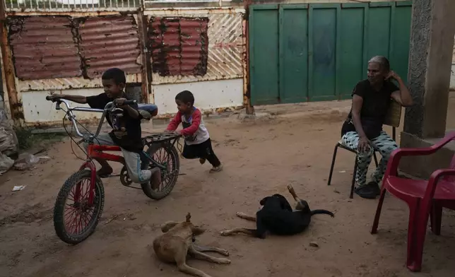 Jorman Romero, one of five children who returned to Venezuela from Mexico with their parents after abandoning plans to reach the United States amid President Donald Trump's migration crackdown, is pushed on a bike by his brother under the watchful eye of their grandmother in Maracaibo, Venezuela, Monday, June 16, 2025. (AP Photo/Matias Delacroix)