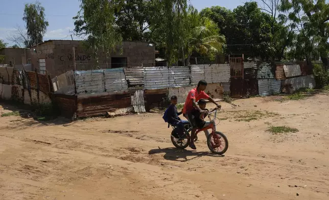 Jolber Romero, one of five children who returned to Venezuela from Mexico with their parents after abandoning plans to reach the United States amid President Donald Trump's migration crackdown, pedals his two younger brothers to school in Maracaibo, Venezuela, Monday, June 16, 2025. (AP Photo/Matias Delacroix)
