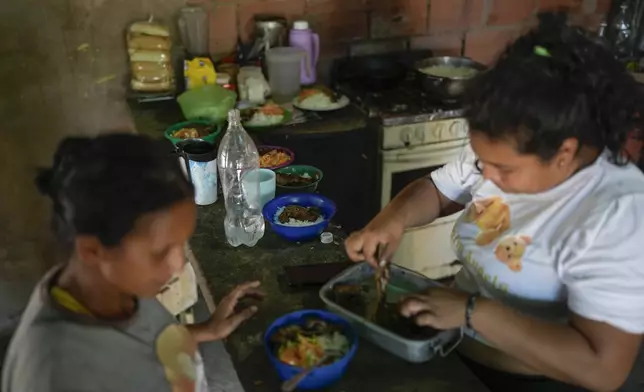 Yoselin Perez, left, who returned to Venezuela from Mexico with her husband and five children after abandoning plans to reach the United States amid President Donald Trump's migration crackdown, dishes up lunch bowls with the help of a neighbor in Maracaibo, Venezuela, Monday, June 16, 2025. (AP Photo/Matias Delacroix)