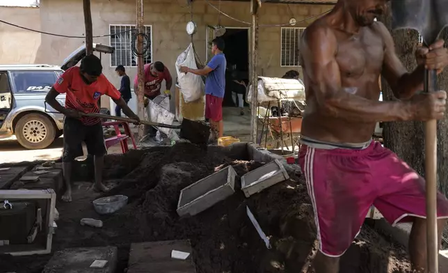 Jolber Romero, left, one of five children who returned to Venezuela from Mexico with his parents after abandoning plans to reach the United States amid President Donald Trump's migration crackdown, shovels sand into molds to cast aluminum pots, in Maracaibo, Venezuela, Monday, June 16, 2025. (AP Photo/Matias Delacroix)