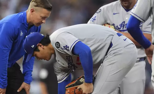 Los Angeles Dodgers starting pitcher Shohei Ohtani, right, is tended to by a trainer after being hit by an RBI single off the bat of Colorado Rockies' Orlando Arcia in the fourth inning of a baseball game, Wednesday, Aug. 20, 2025, in Denver. (AP Photo/David Zalubowski)