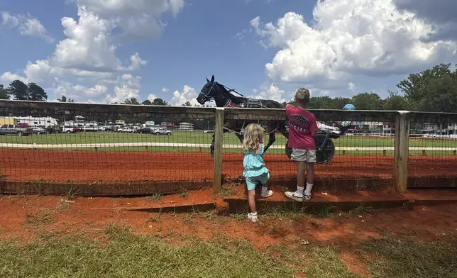 Two kids stand near the racetrack at the Neshoba County Fair and watch as a horse trots past on Wednesday, July 30, 2025 in Philadelphia, Miss. (AP Photo/Sophie Bates)