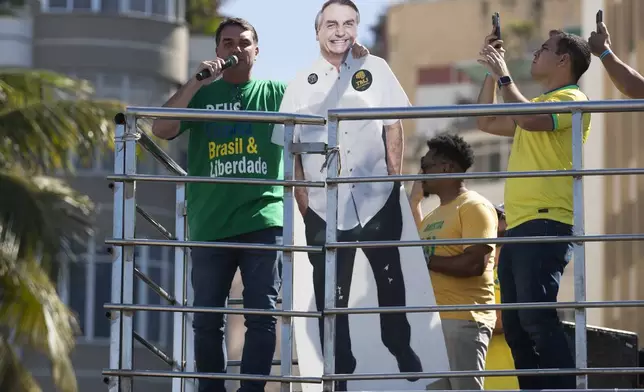 Senator Flavio Bolsonaro speaks while embracing a cutout of his father, former President Jair Bolsonaro, during a demonstration to protest a Supreme Court trial in which Jair Bolsonaro faces charges for alleged involvement in a 2022 coup attempt, at Copacabana Beach in Rio de Janeiro, Sunday, Aug. 3, 2025. (AP Photo/Bruna Prado)